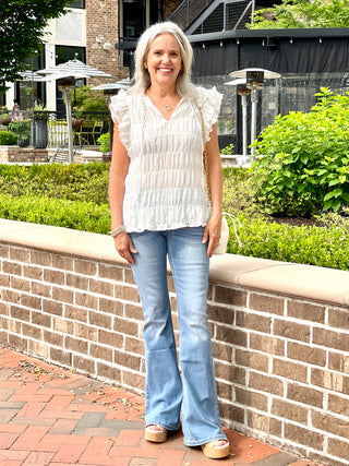 a white boxy cut v neck top with a self tie and soft textured fabric worn with blue jeans