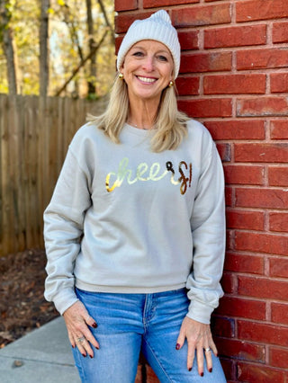 a sand colored crewneck sweatshirt with a golden cheers emblem