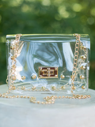 a gold studded clear handbag with a glamorous gold closure perfect for stadium games and football fashion