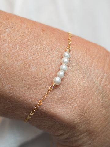 a bar bracelet with white pearls along a gold cable chain