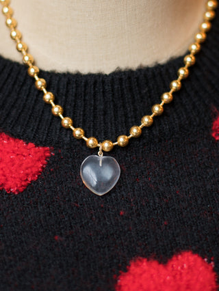 a gold beaded necklace with a glass heart charm