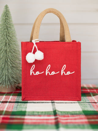 a red christmas present bag that reads ho ho ho with white pom poms perfect for holiday home decor and host gifts