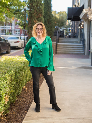a long sleeve ruffled blouse in emerald green featuring smooth satin fabric and a flattering fit shown with black pants