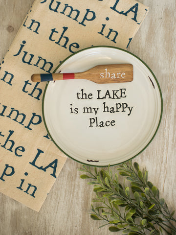 a white stoneware appetizer plate reading the lake is my happy place with a wooden boat oar spreader reading share