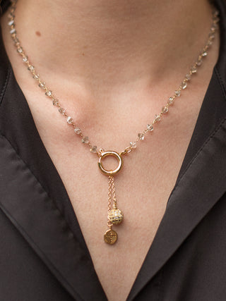 a gold statement necklace with crystals along the chain and two charms featuring a gold ball and stamped cross on a disc