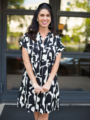 a black and white print dress with short sleeves and pleats featuring a knee length hem