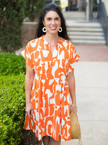 a bright orange and white print dress with short sleeves and pleats featuring a knee length hem