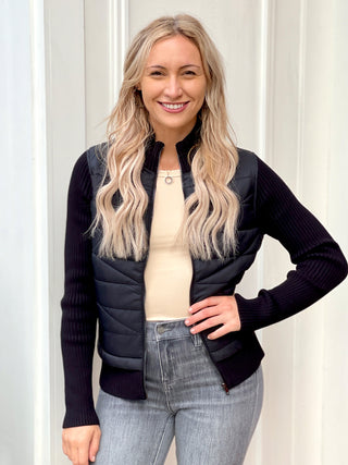 a black zip front jacket with puff material and ribbed sweater knit sleeves perfect for form fitting winter wear and sports