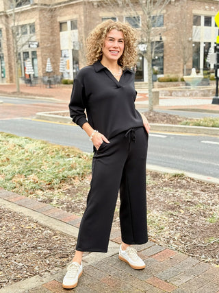 a black long sleeve pull over collared sweater with black wide leg pants 