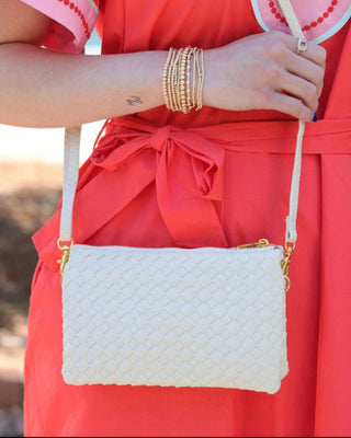 Person wearing a red dress with gold bangles holding a white textured handbag.