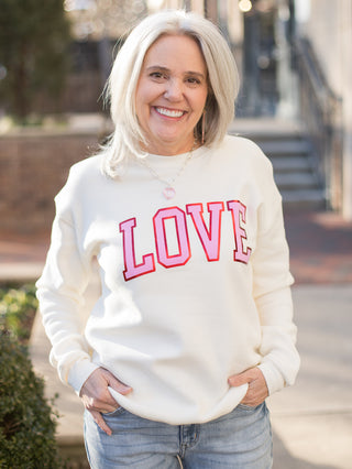 a cream valentines sweatshirt that reads love in pink and red vintage text
