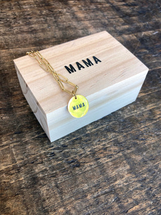 a gold chain link necklace with a round pendant that reads Mama on top of a wooden jewelry box engraved with mama