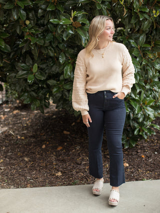 a light beige sweater with long statement sleeves and romantic ruffles featuring a high scoop neckline shown with black jeans