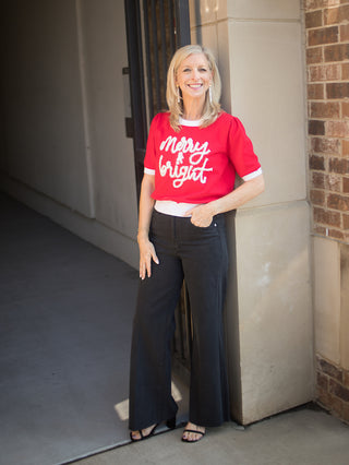 a short sleeve christmas sweater in red and white that reads merry and bright perfect for holiday gifts with black pants