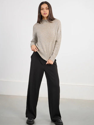 a beige metallic long sleeve knitted sweater with a high ribbed collar worn with black pants