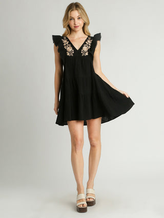 black tiered mini dress with playful ruffle sleeves and embroidered flower details worn with neutral sandals