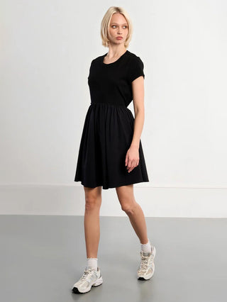 Woman wearing a black dress with white sneakers on a plain background