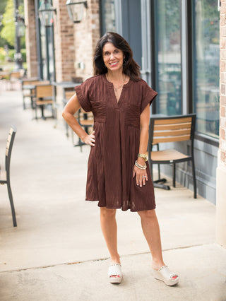 a brown mini dress with short sleeves and a relaxed fit perfect for warm autumn days shown with beige slides