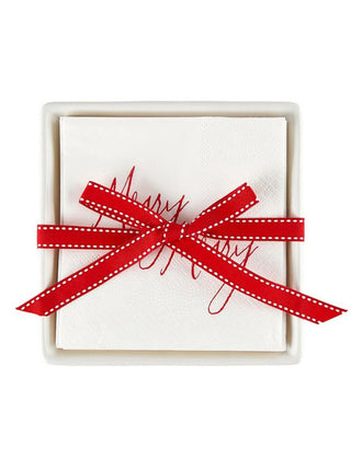 a white ceramic napkin tray with merry christmas napkins tied in a red bow