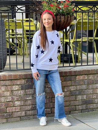 cozy white sweatshirt adorned with dark blue embroidered stars and the words oh my stars worn with blue jeans