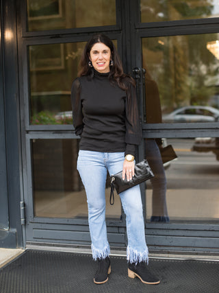 a black mock turtleneck with see through balloon statement sleeves great for any capsule wardrobe shown with fringe jeans