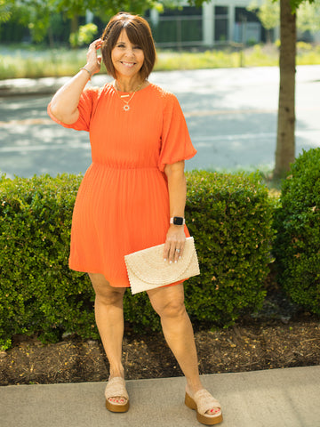 an orange above the knee dress with short puff sleeves and an open back tie in soft textured fabric shown with beige slides