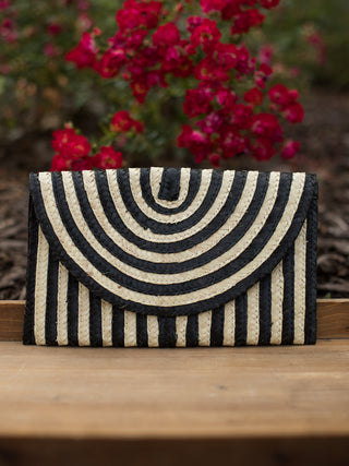 a straw clutch bag in black and white rattan with a magnetic snap closure