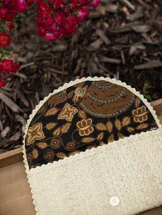 a straw clutch bag in ivory rattan with a magnetic snap closure and batik print interior lining