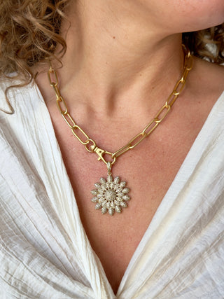 a large gold paperclip chain necklace with a sparkling flower pendant