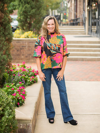 a moody floral print blouse with jewel tones and black featuring statement puff sleeves shown with denim pants