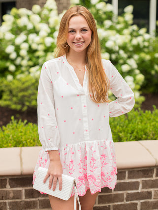 a white dress featuring hot pink embroidery with three quarter lengths sleeves and a scalloped short hem