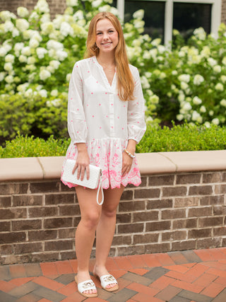a white dress featuring pink embroidery with three quarter lengths sleeves and a scalloped short hem shown with white slides