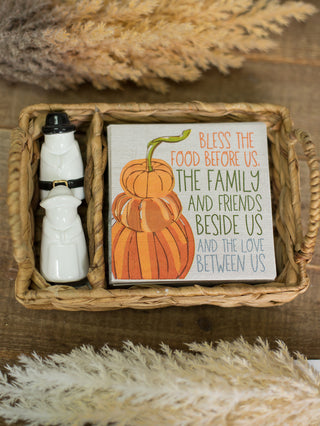 a thanksgiving host gift with pilgrim salt and pepper shakers and fall decor napkins inside a woven display basket