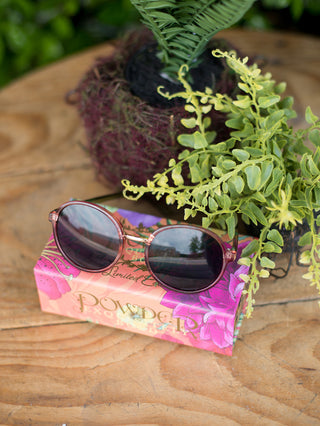 circular vintage shape sunglasses with rose colored frames on top of its complimentary floral case