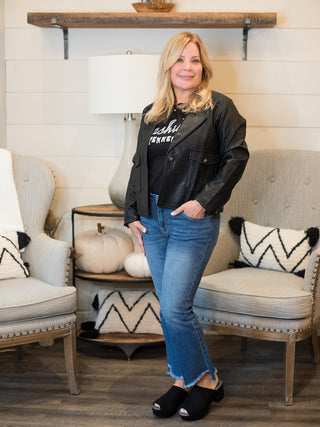 a black faux leather crop jacket with button closures great for layering in cold weather months shown with denim pants