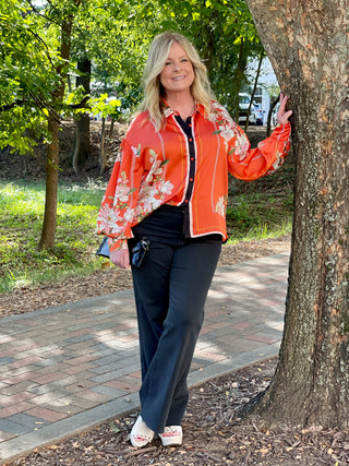 a relaxed fit orange button down top with long sleeves and flower details and stripes in slinky fabric shown with black pants