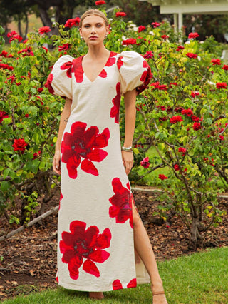 Woman wearing a white dress with red floral patterns in a garden setting
