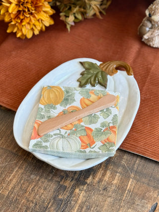 white pumpkin ceramic plate with wood knife and a set of white square napkins