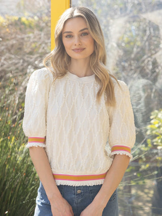 chic cream patterned knit top with a vibrant orange and pink detail at the hem and cuffs