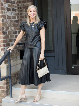 a black pleated midi skirt in faux leather with a high rise cut great for day to night looks shown with black puff sleeve top