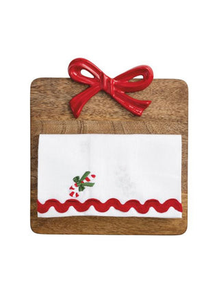 a holiday cutting board with a red iron ribbon and a white christmas tea towel