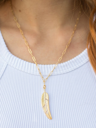 a 24k gold necklace with a paper clip chain adorned with a gold feather charm with a rhinestone spine