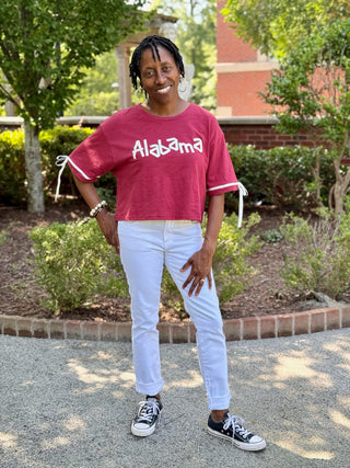 a crimson red alabama rally top with dainty ribbons on the sleeves worn with white jeans