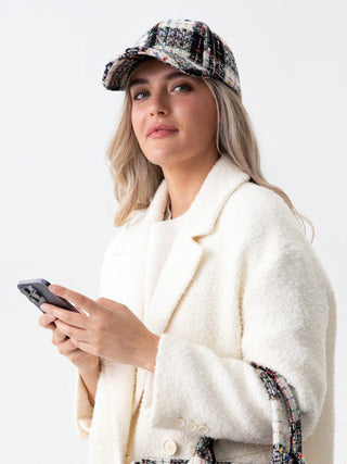 a black and white plaid boucle fabric sports cap worn with a white jacket