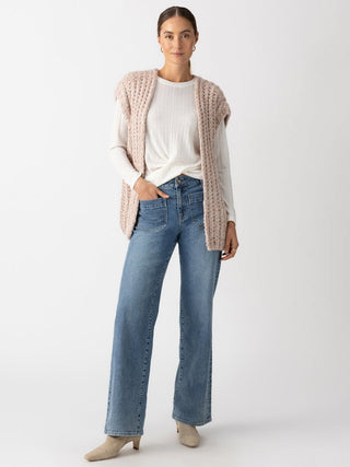 a comfortable chunky open front sweater vest made with cream and taupe marl yarn worn over a white long sleeve