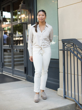 an ivory satin button down blouse that ties at the waist perfect for summer to fall dressing shown with white pants