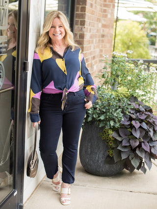 a multicolor blouse in jewel tones with a tie at the waist perfect for transitional dressing shown with white heels