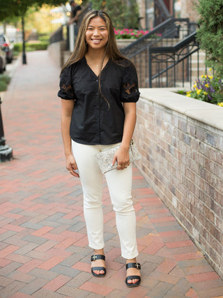 a black puff sleeve top with lace details and buttons down the front shown with white pants
