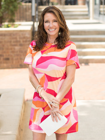 a short sleeve mini dress with an orange pink and red patterned design and an open back