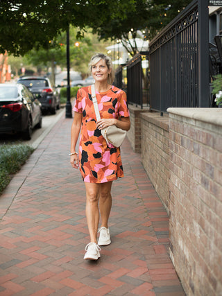 a patterned short sleeve dress with orange and pink accents featuring an open back shown with ivory sneakers